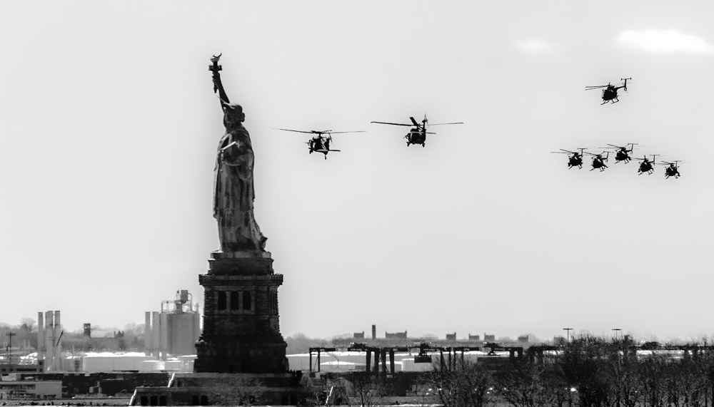 Photo shows Statue of Liberty and eight military helicopters flying toward the statue. the image symbolizes threatening to democracy.